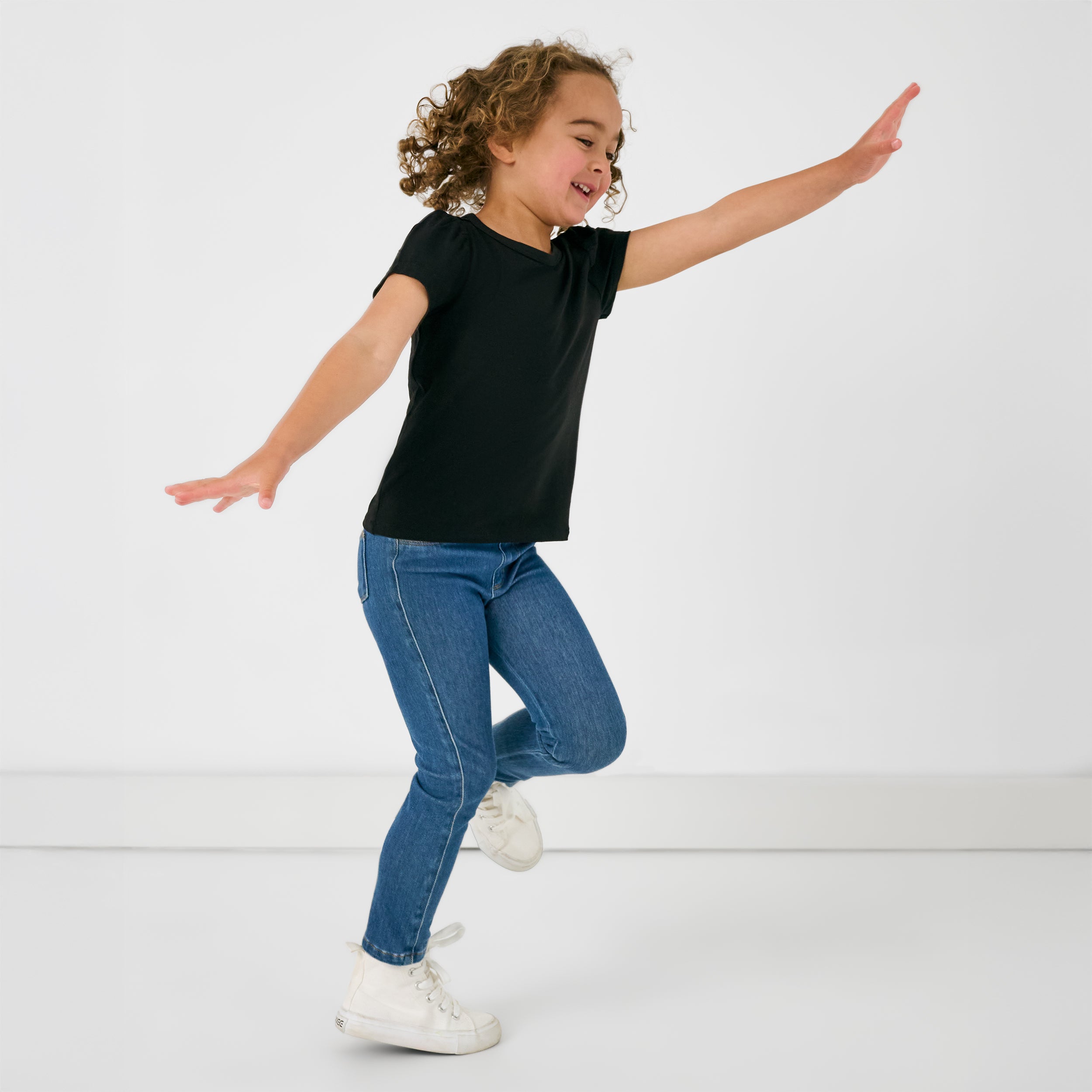 Child in motion wearing the Black Puff Sleeve Tee and Midwash Blue Denim Jegging