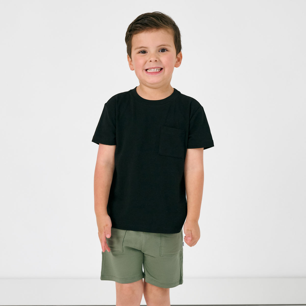 Standing boy wearing the Black Short Sleeve Relaxed Pocket Tee with green shorts 