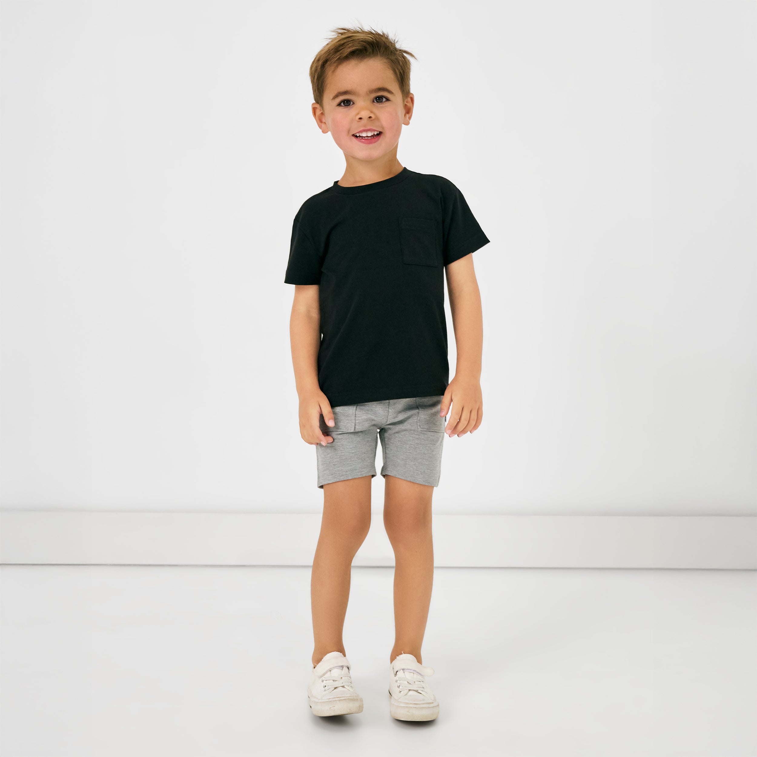 Standing child wearing the Black Short Sleeve Relaxed Pocket Tee with gray shorts 
