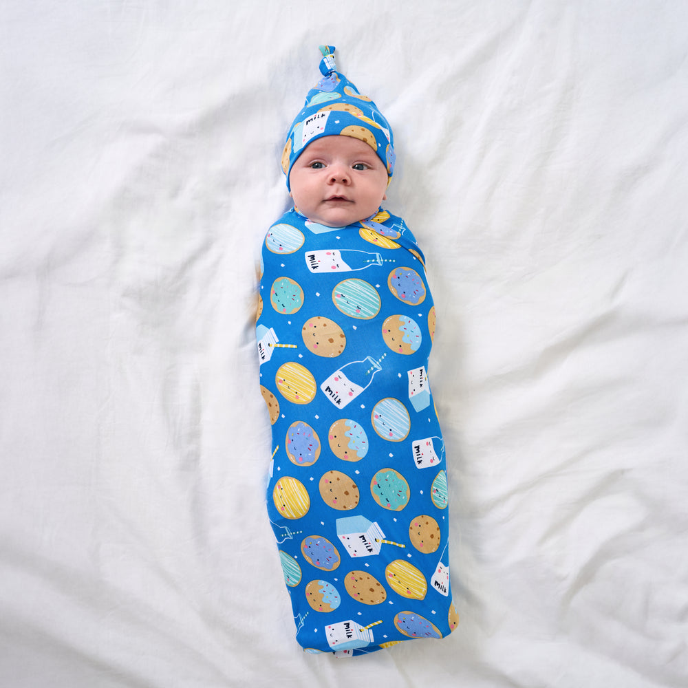 Aerial view of baby wearing the Blue Cookies & Milk Swaddle & Hat Set