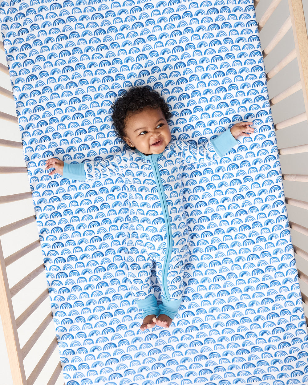 Baby laying on the Blue Rainbows Fitted Crib Sheet