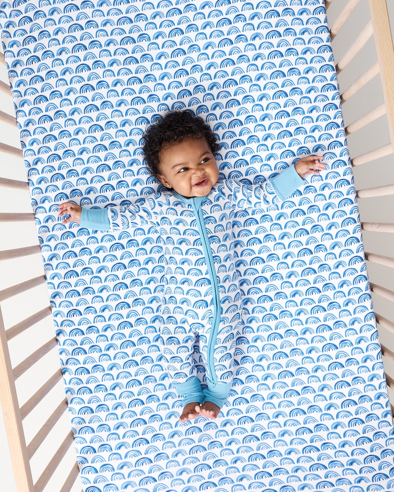 Baby laying on the Blue Rainbows Fitted Crib Sheet