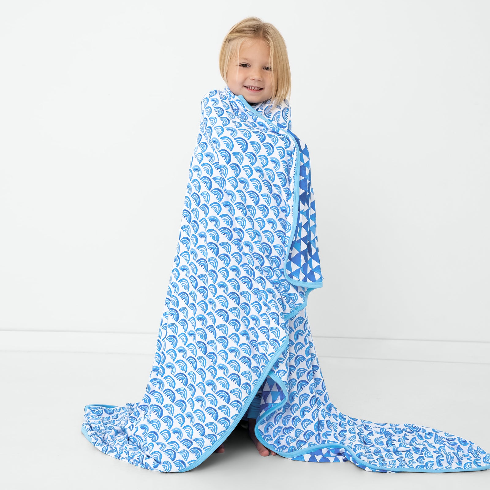 Standing child wrapped in the Blue Rainbows Large Cloud Blanket®
