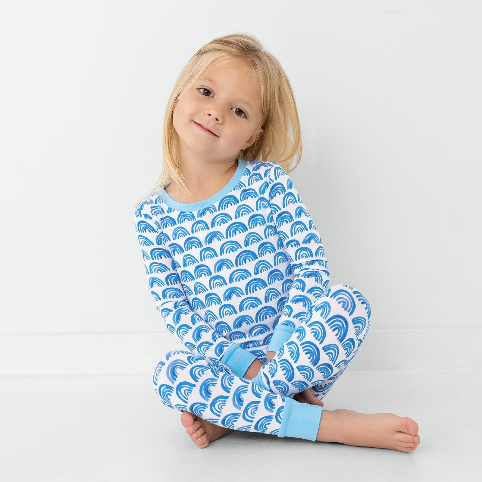 Sitting child wearing the Blue Rainbows Two-Piece Pajama Set