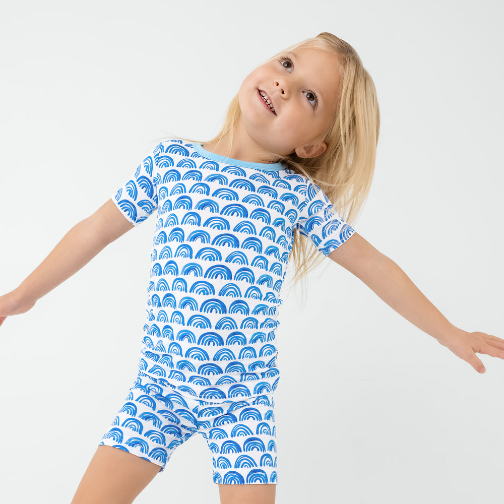 Posing child wearing the Blue Rainbows Two-Piece Short Sleeve & Shorts Pajama Set