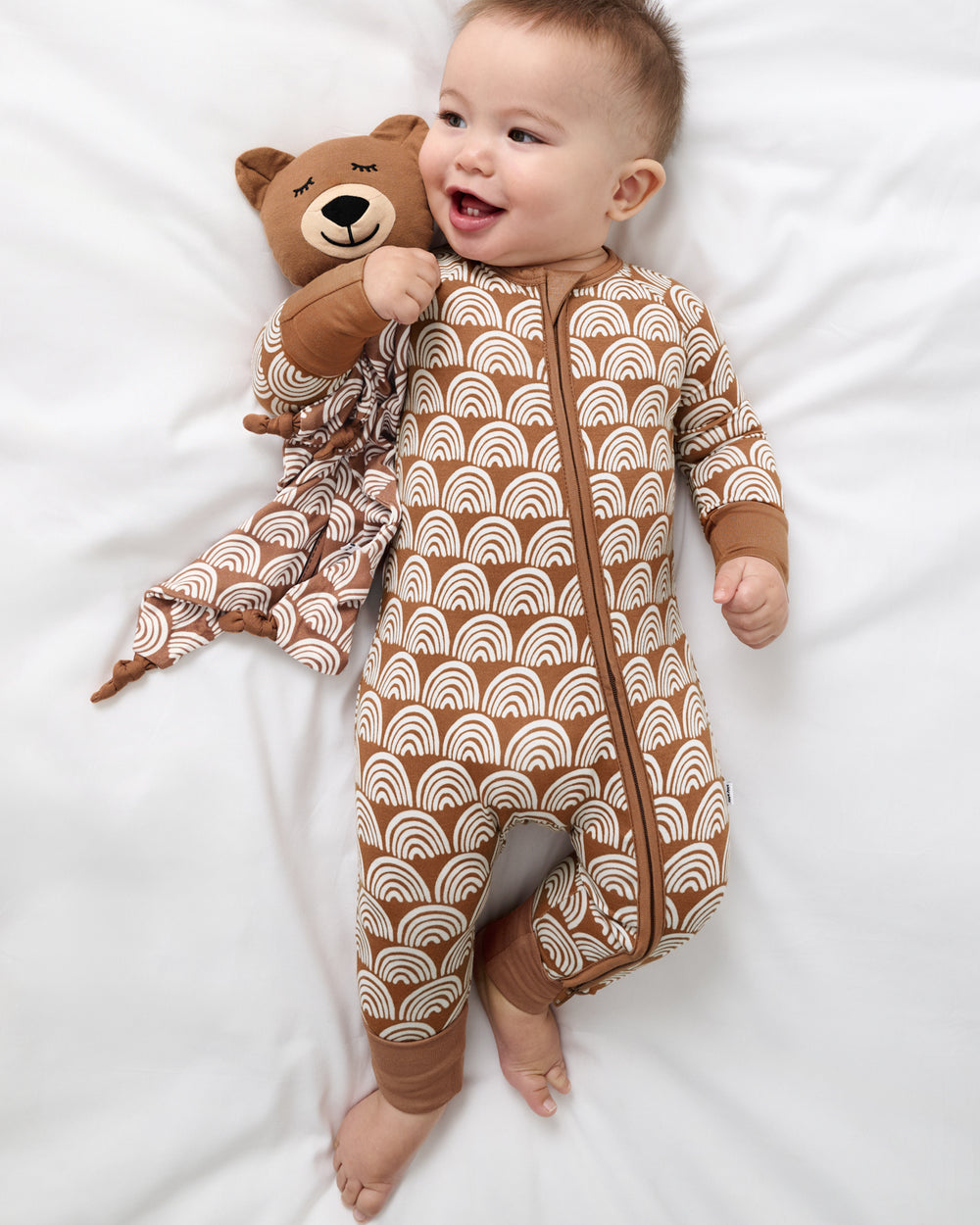 Aerial view of baby laying with the Bowie the Bear Sleepyhead Lovey wearing a matching footie