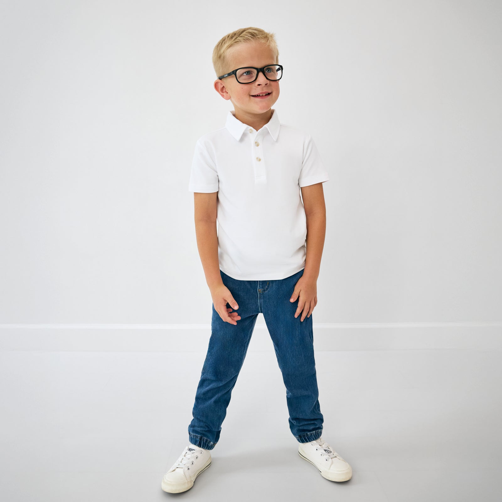 Standing child wearing the Bright White Polo Shirt with blue denim joggers