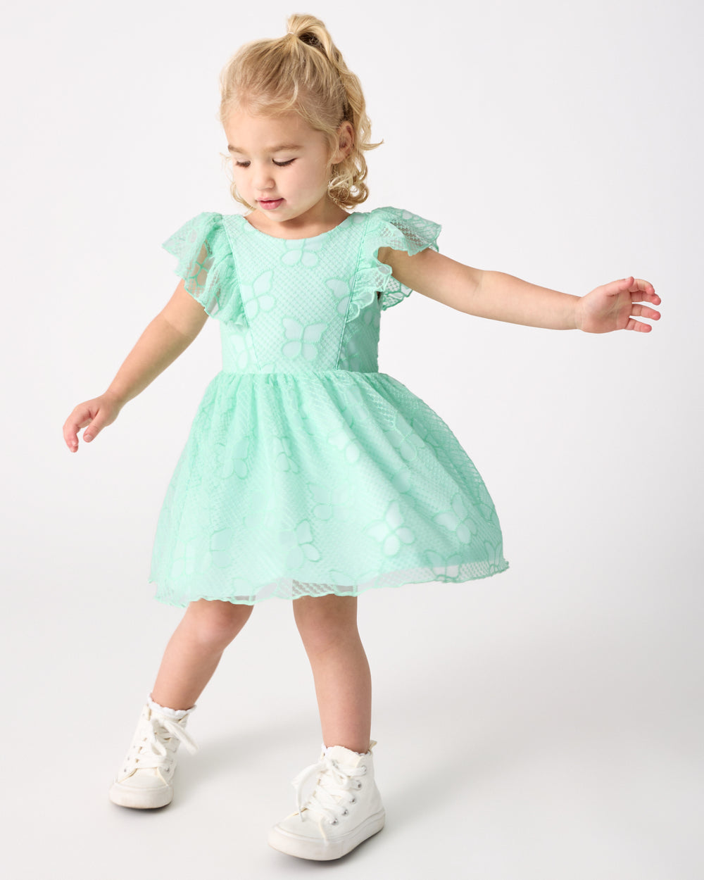 Girl wearing the Butterfly Brook Smocked Flutter Dress with white sneakers