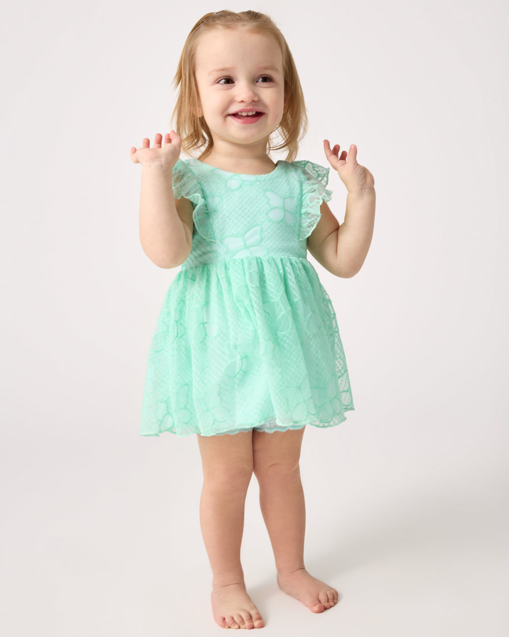 Standing toddler wearing the Butterfly Brook Smocked Flutter Dress with Bloomer