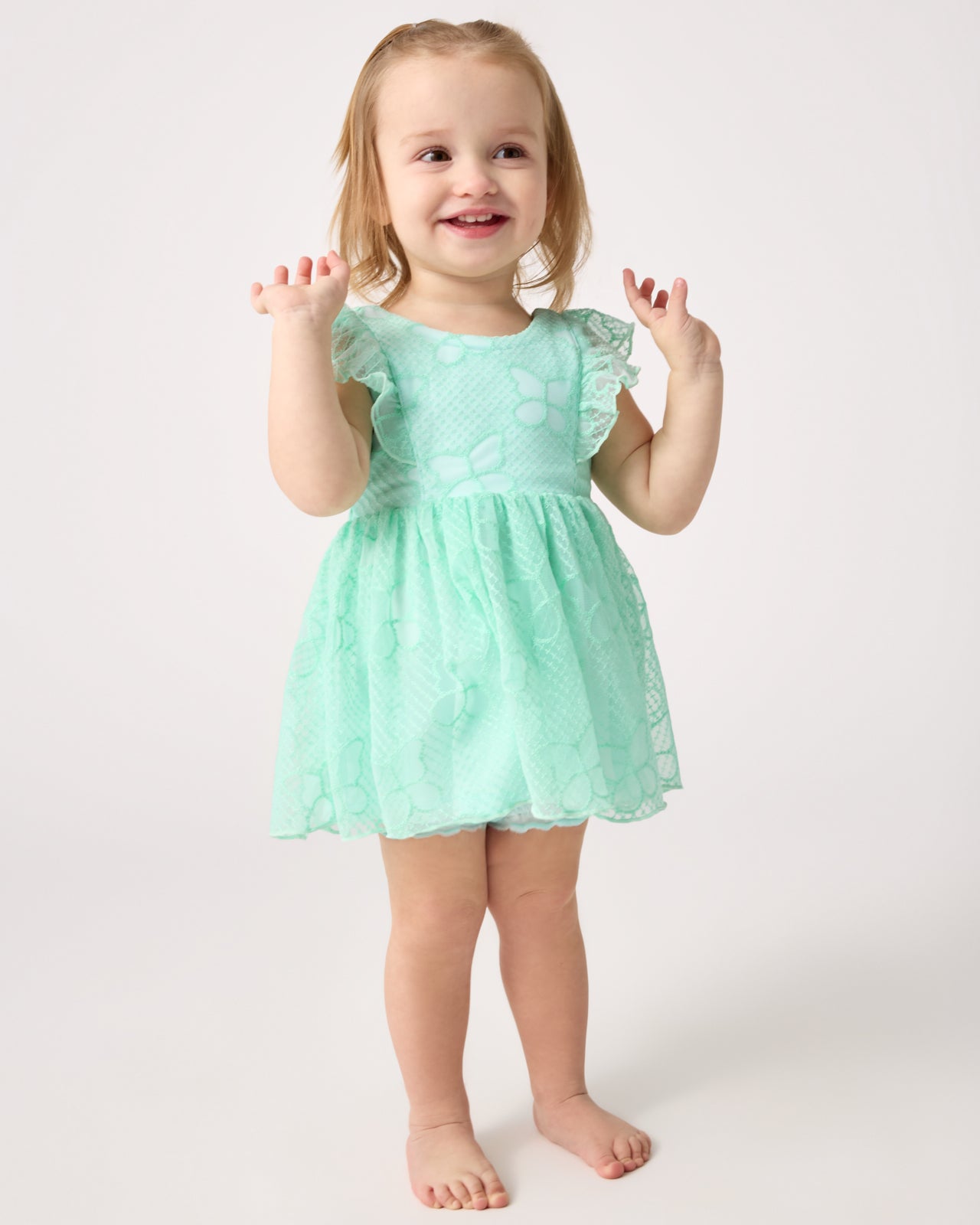 Standing toddler wearing the Butterfly Brook Smocked Flutter Dress with Bloomer