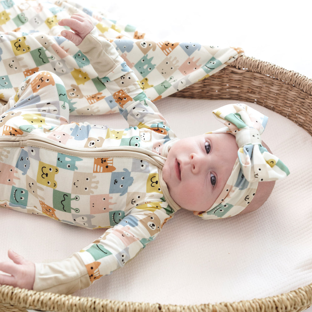 baby laying in basket wearing the check mates zippy, next to a blanket and wearing the matching luxe bow.