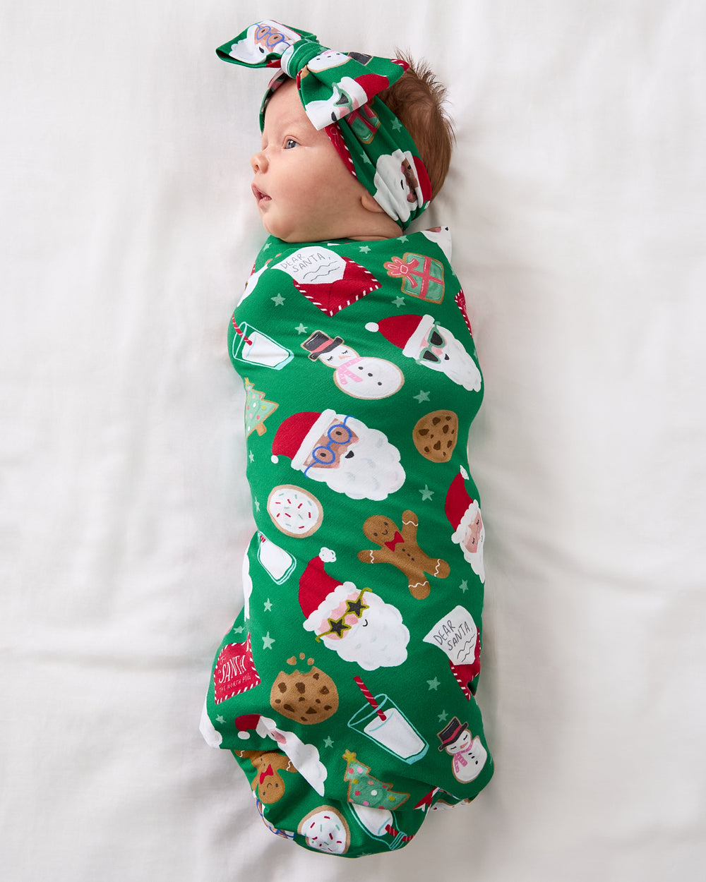 Aerial view of baby wearing the Cookies for Santa Swaddle & Luxe Bow Headband Set