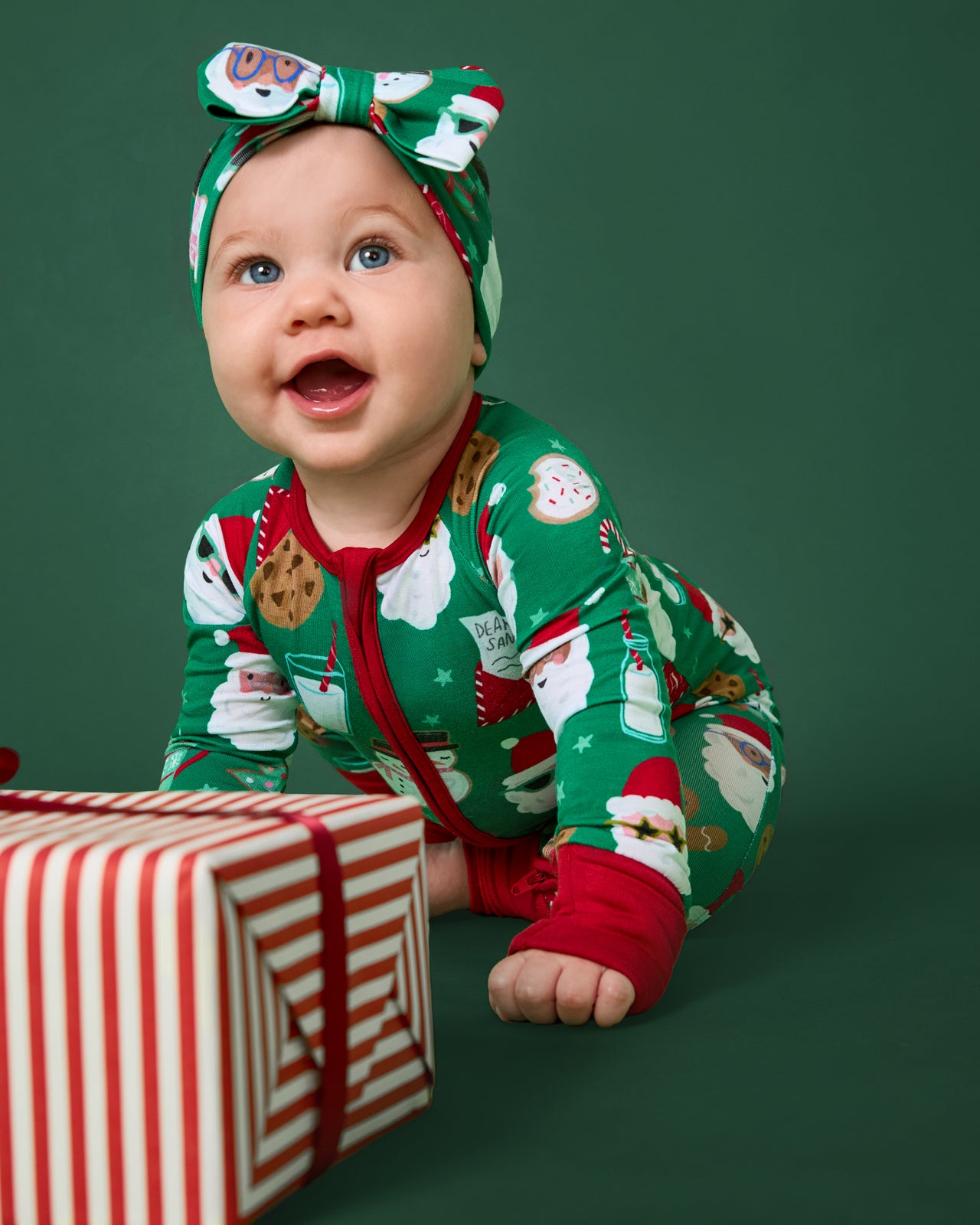 Crawling baby wearing the Cookies for Santa Zippy on a green background