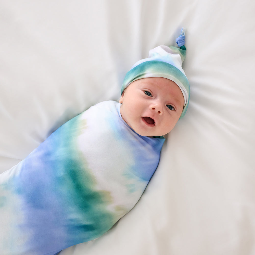 Alternate aerial view of baby wearing the Blue Cosmic Mist Swaddle & Hat Set