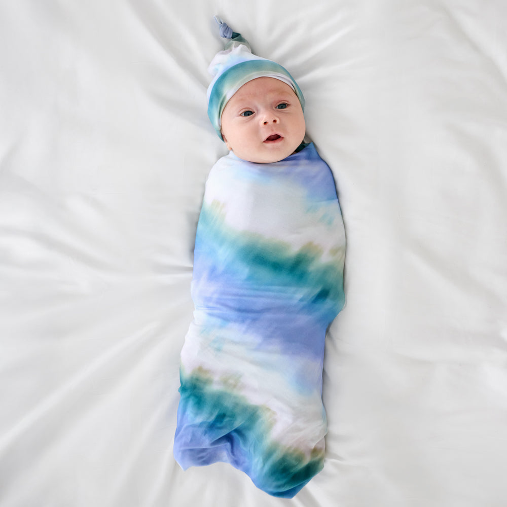 Aerial view of child wearing the Blue Cosmic Mist Swaddle & Hat Set