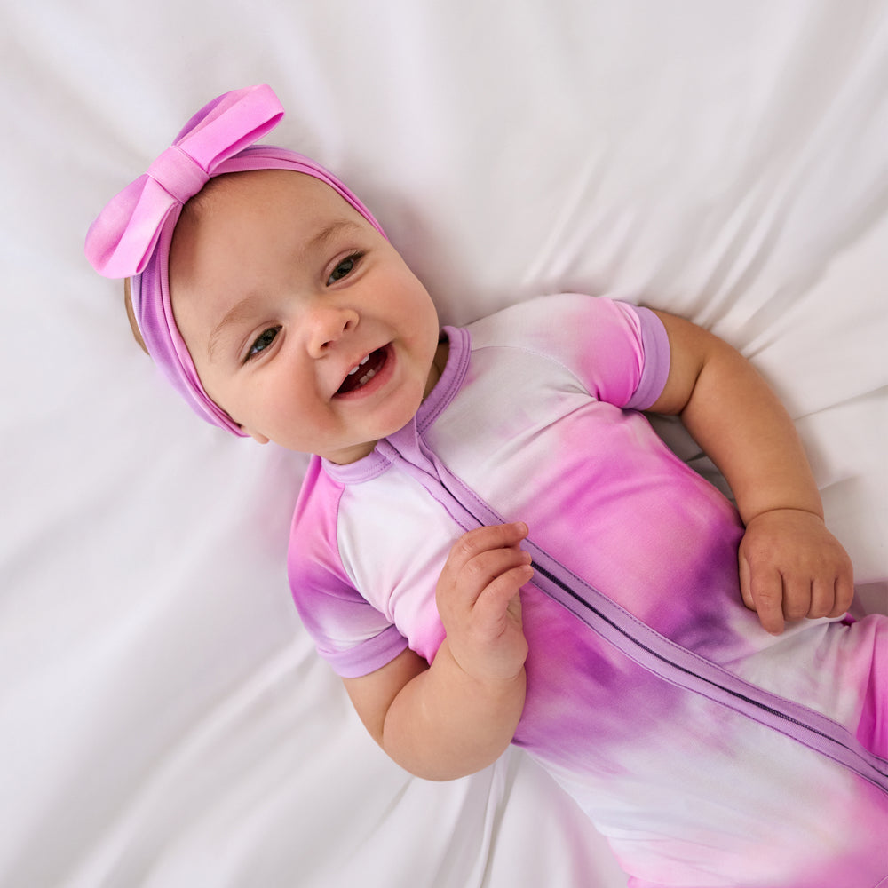 Aerial view of baby wearing the Pink Cosmic Mist Shorty Zippy with a matching baby bow headband