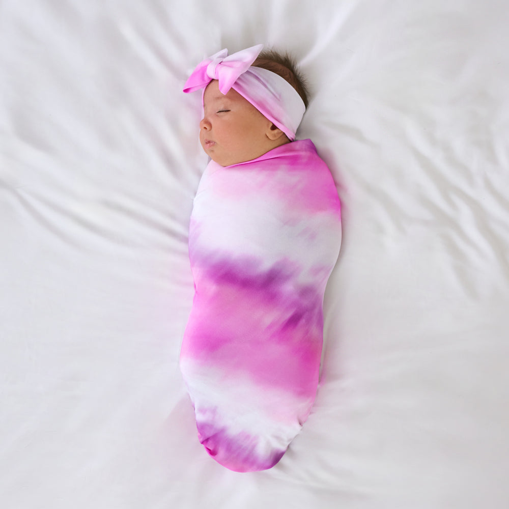 Aerial view of baby swaddled in the Pink Cosmic Mist Swaddle & Luxe Bow Headband Set