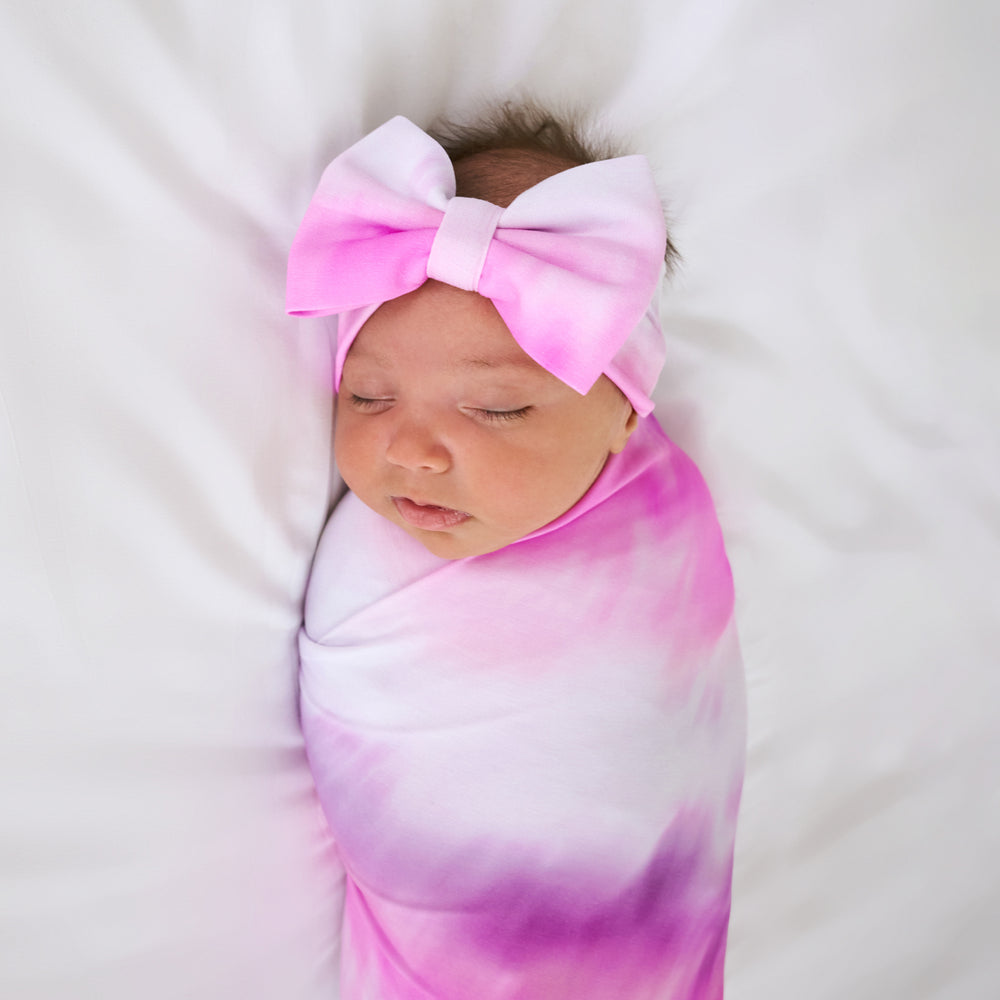 Close up of baby wearing the Pink Cosmic Mist Swaddle & Luxe Bow Headband Set