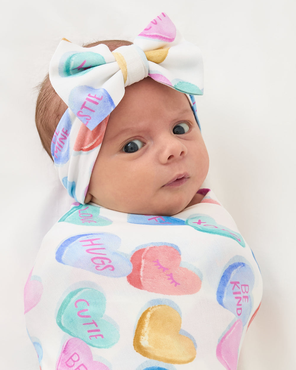 Close up of baby swaddled in the Candy Cuties Swaddle & Luxe Bow Headband Set