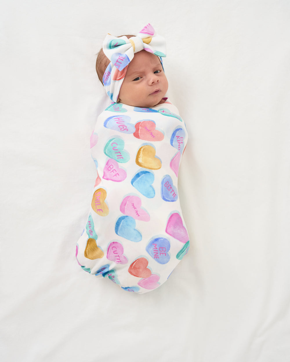 Aerial view of baby swaddled in the Candy Cuties Swaddle & Luxe Bow Headband Set