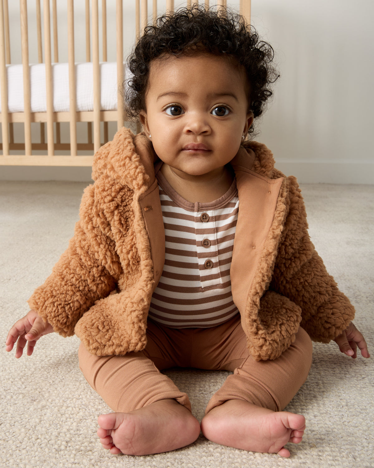 Sitting baby wearing the Chestnut Brown Stripe Henley Bodysuit with leggings and a sherpa jacket