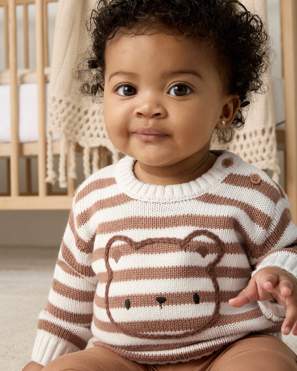 Baby wearing the Chestnut Brown Stripe Bear Sweater in a nursery