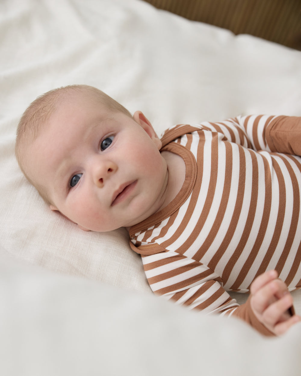 Close up of baby wearing the Chestnut Brown Stripe Crescent Zippy on a white blanket