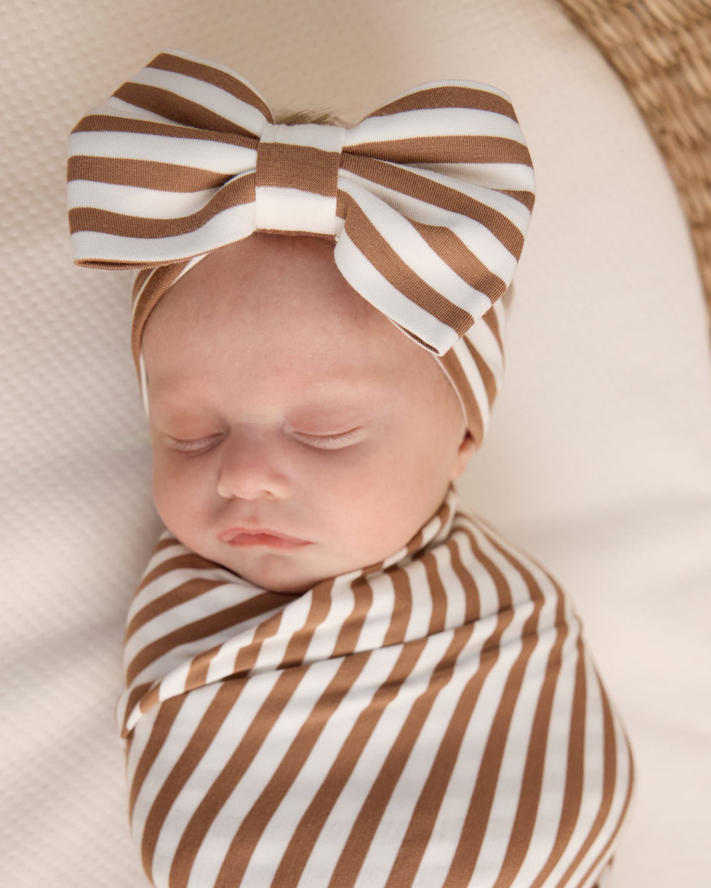 Close up of newborn wrapped in the Chestnut Brown Stripe Swaddle & Luxe Bow Headband Set