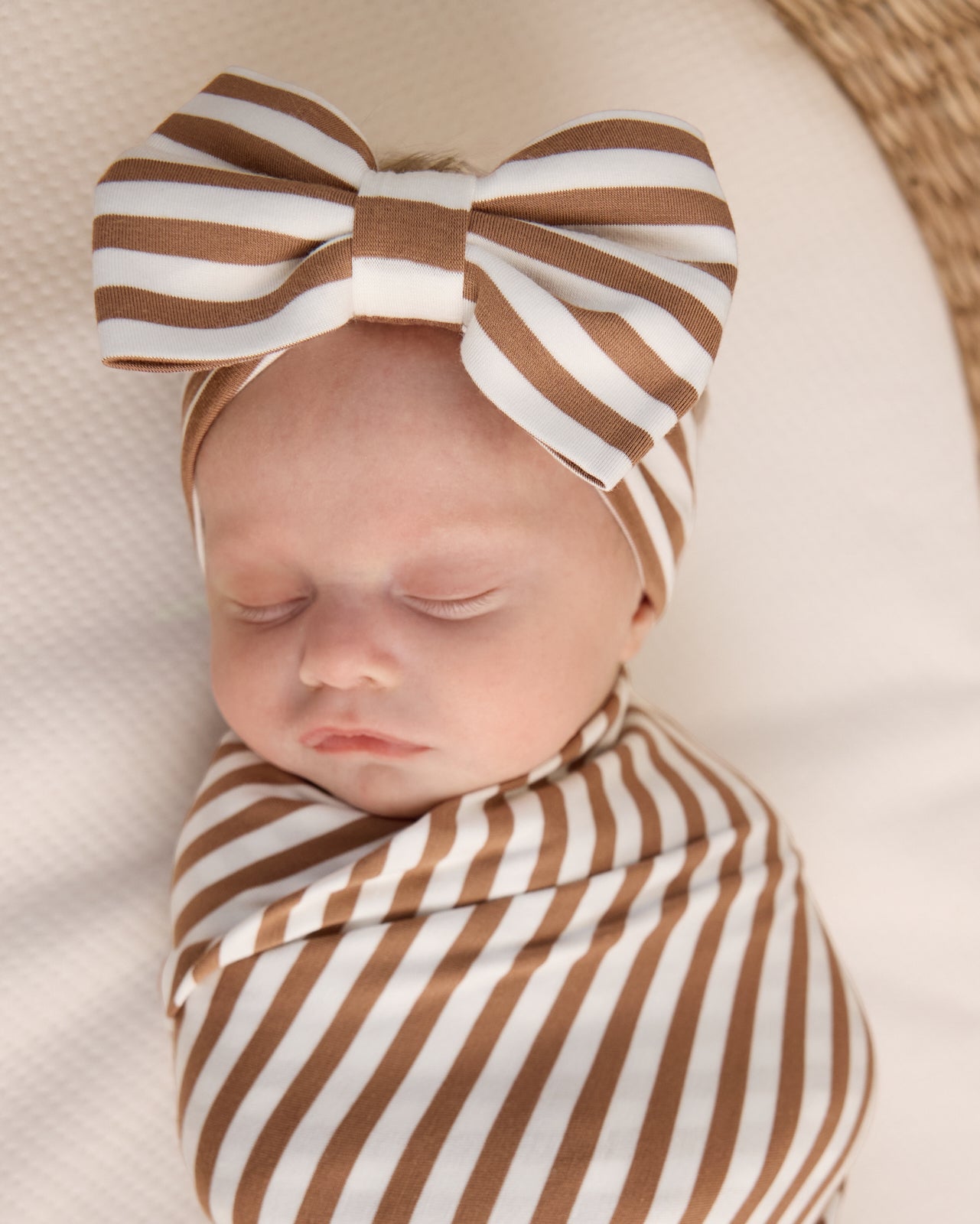 Close up of newborn wrapped in the Chestnut Brown Stripe Swaddle & Luxe Bow Headband Set