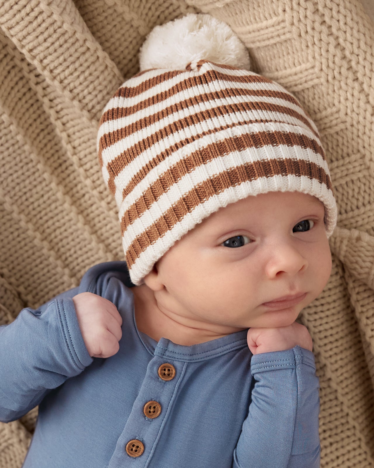 Close up of baby wearing the Chestnut Brown Stripe Sweater Beanie Hat with a blue bodysuit