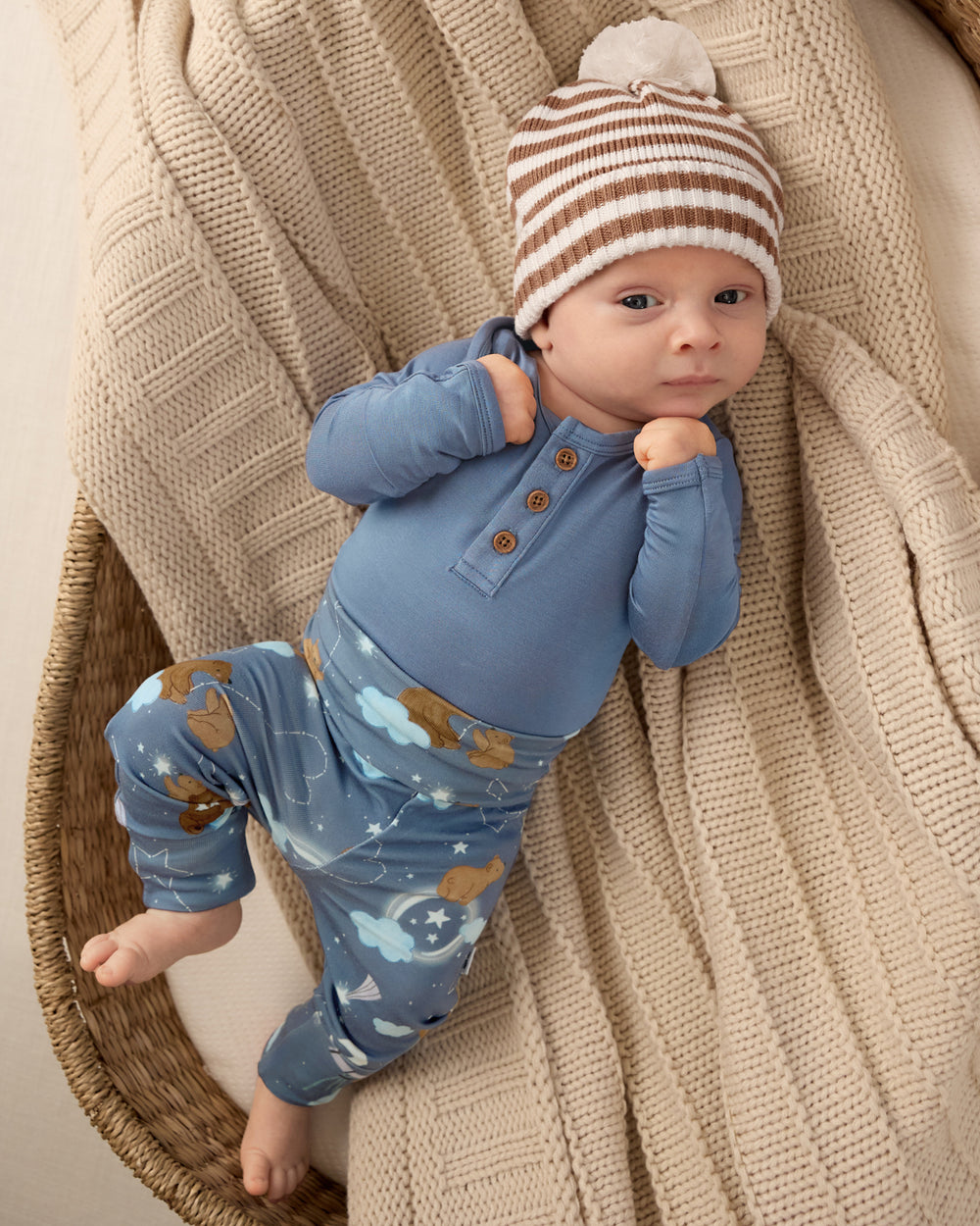 Baby boy wearing the Hazy Blue Henley Bodysuit on a tan knit blanket