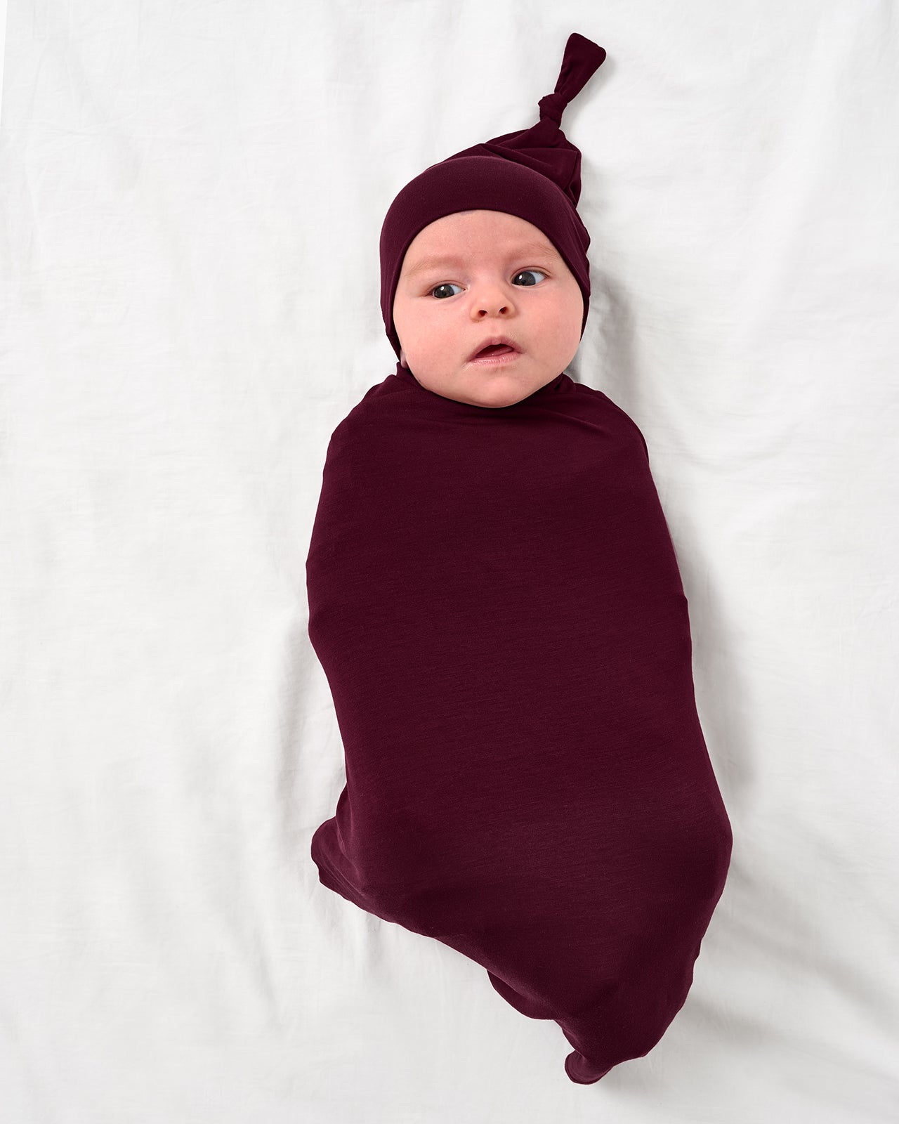 Aerial view of baby wearing the Classic Burgundy Swaddle & Hat Set