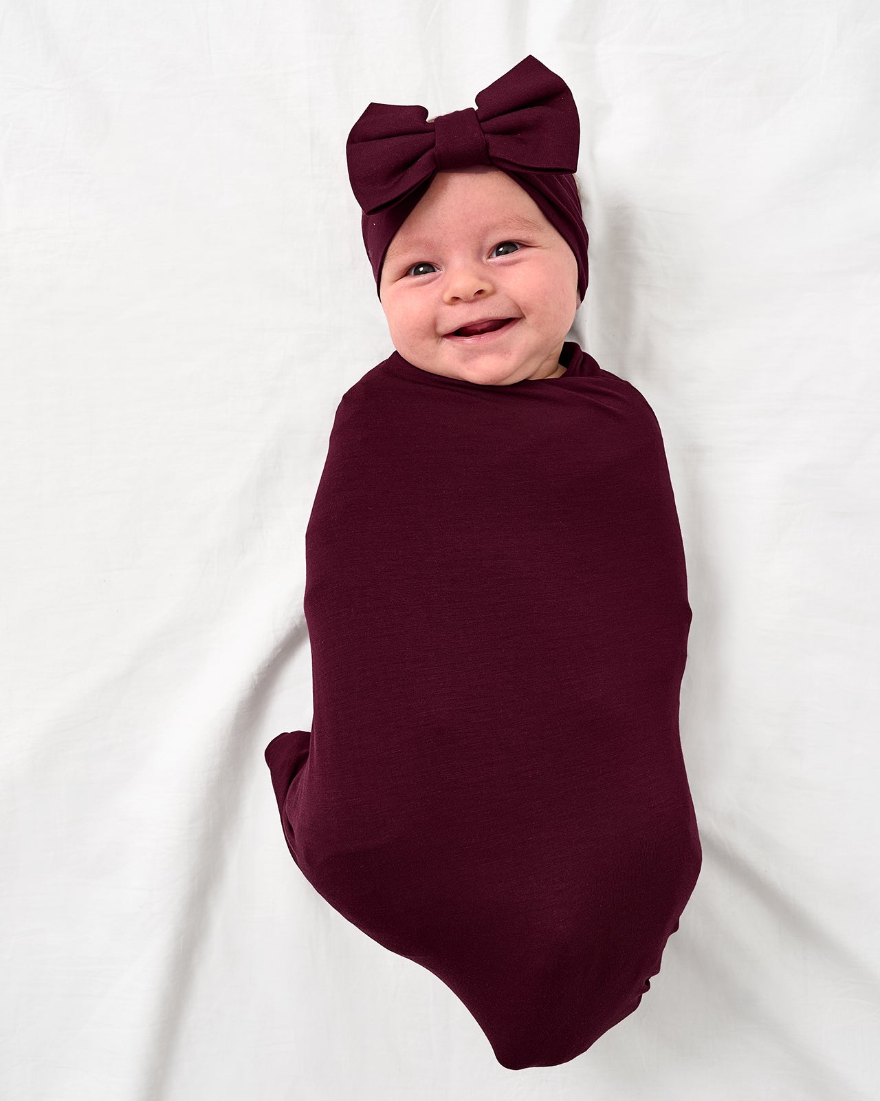 Aerial view of baby wearing the Classic Burgundy Swaddle & Luxe Bow Headband Set