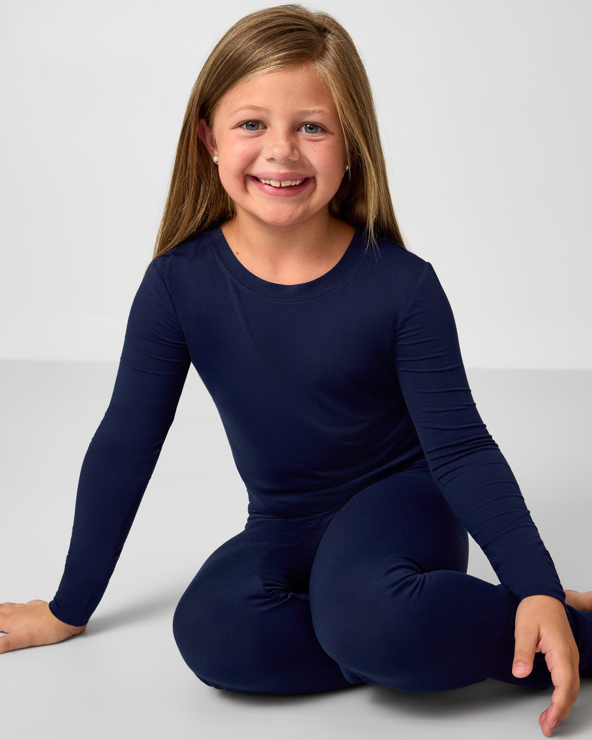 Young girl wearing a navy blue long-sleeve top and pants sitting on a light gray background