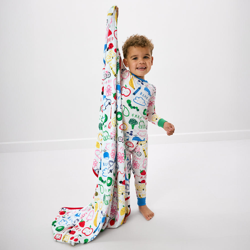 Standing child holding up the Coloring Crew Large Cloud Blanket® wearing the matching two piece pj set