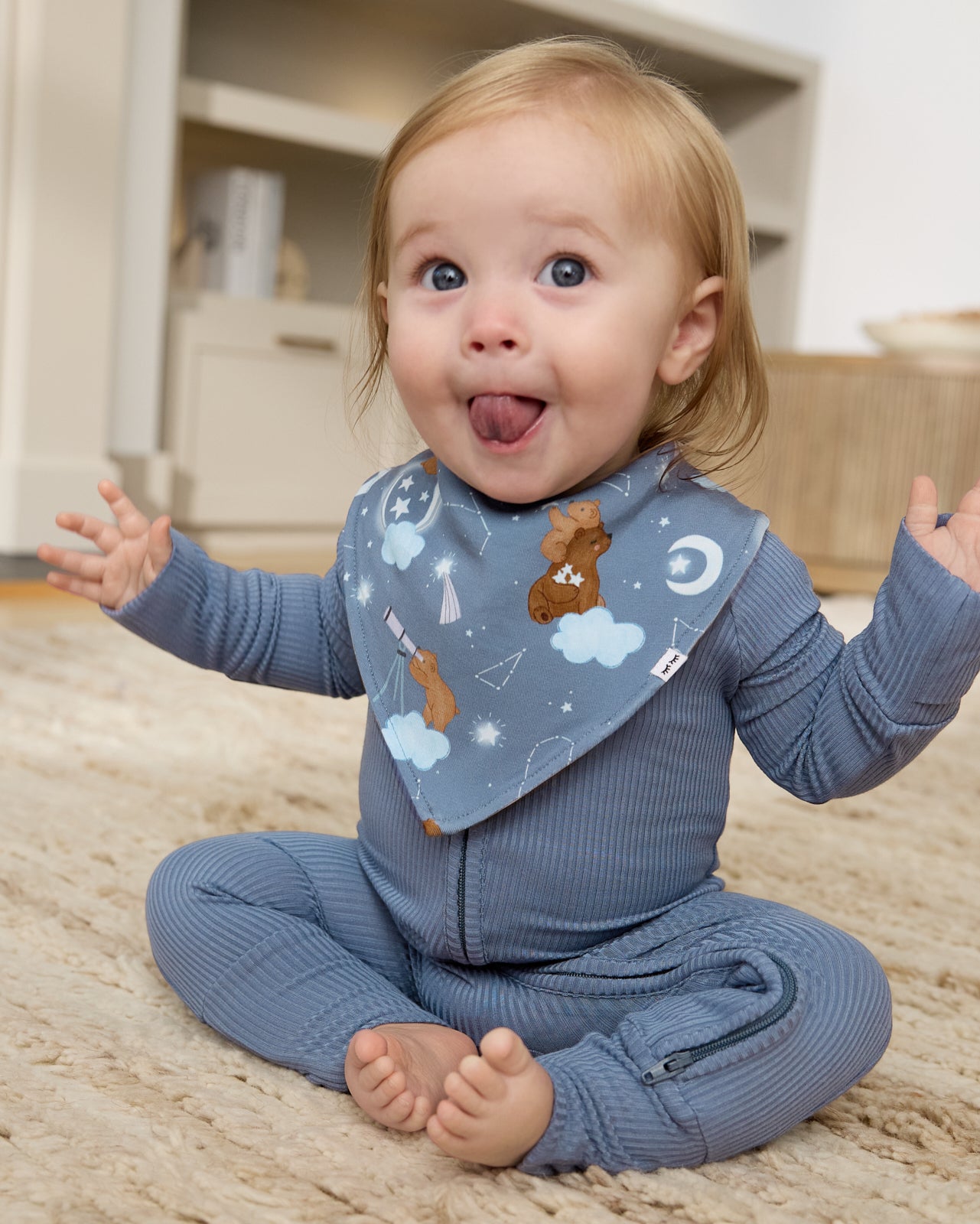 Sitting baby wearing the Constellation Cubs Bandana Bib with a blue zipper pajama
