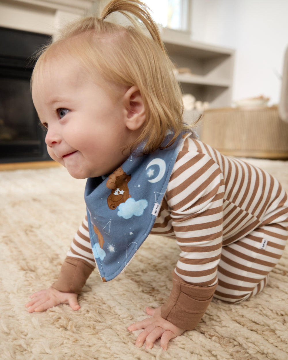 Crawling baby wearing the Constellation Cubs Bandana Bib with a striped zipper pajama
