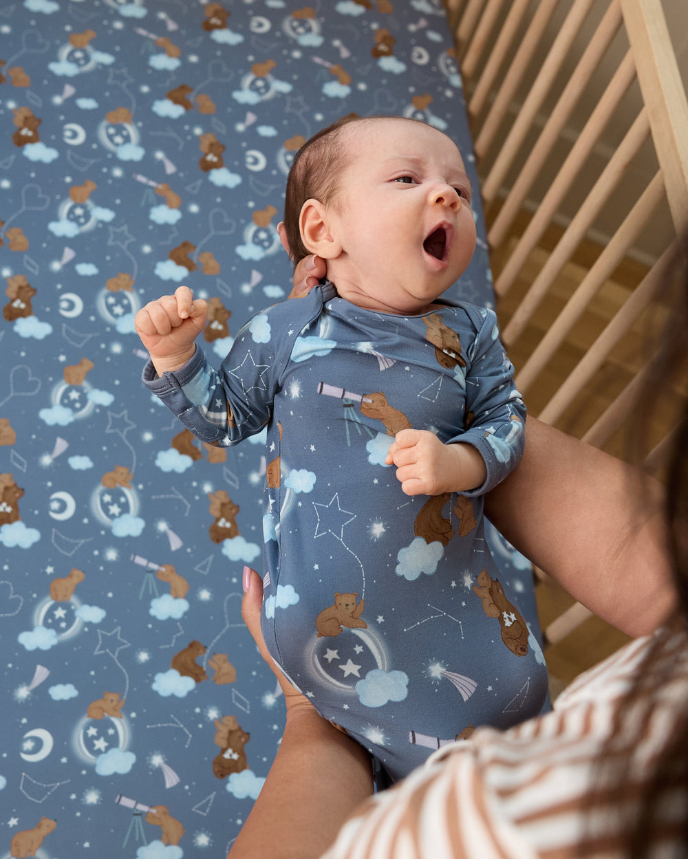 Newborn wearing the Constellation Cubs Infant Gown being put into a crib
