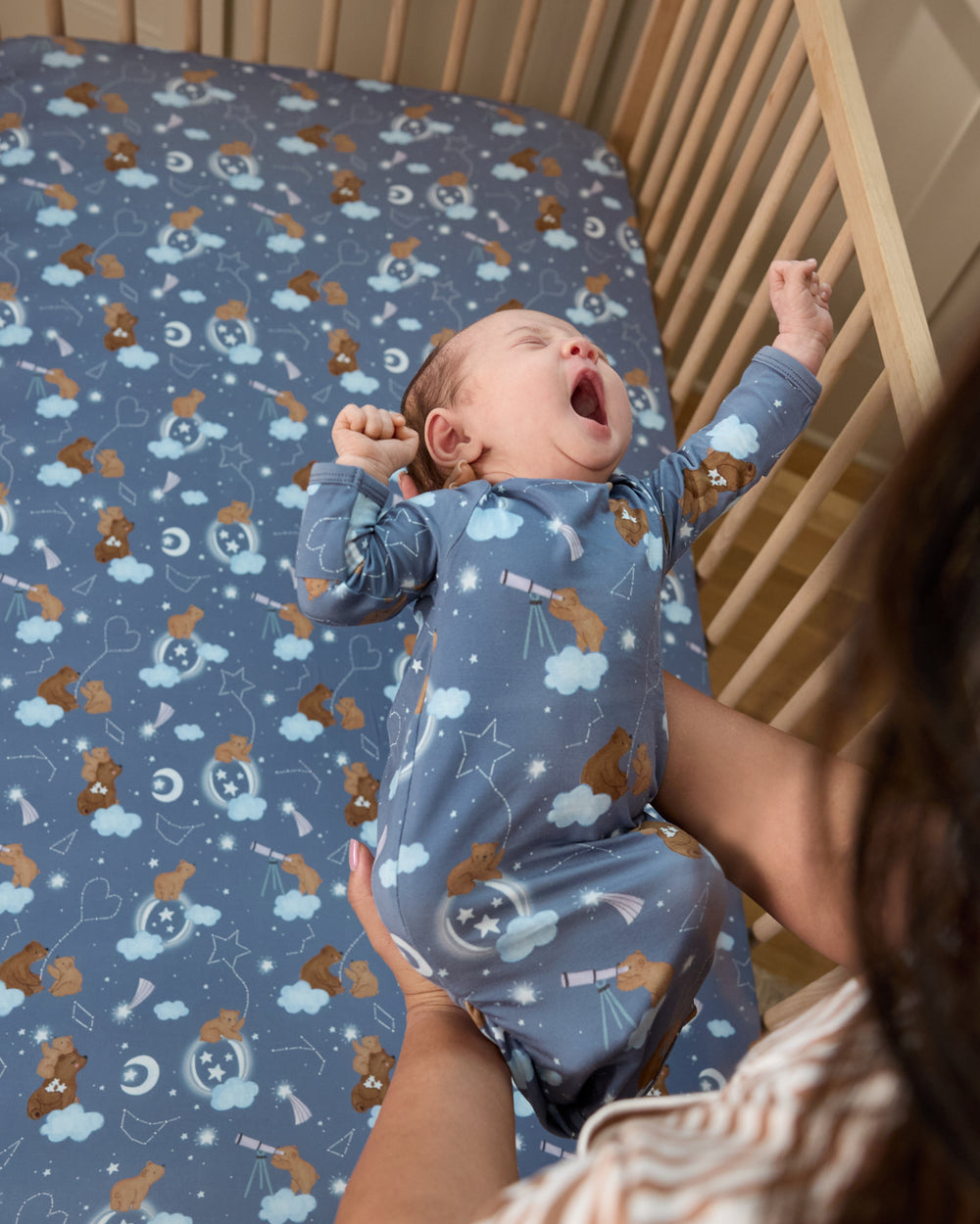 Baby being put into a crib with the Constellation Cubs Fitted Crib Sheet