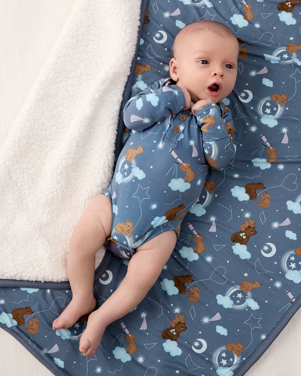 Aerial view of baby wearing the Constellation Cubs Henley Bodysuit on the matching Cloud Blanket