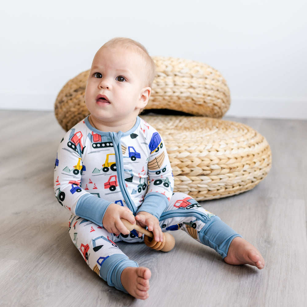 Baby sitting wearing the construction zippy and holding a rattle