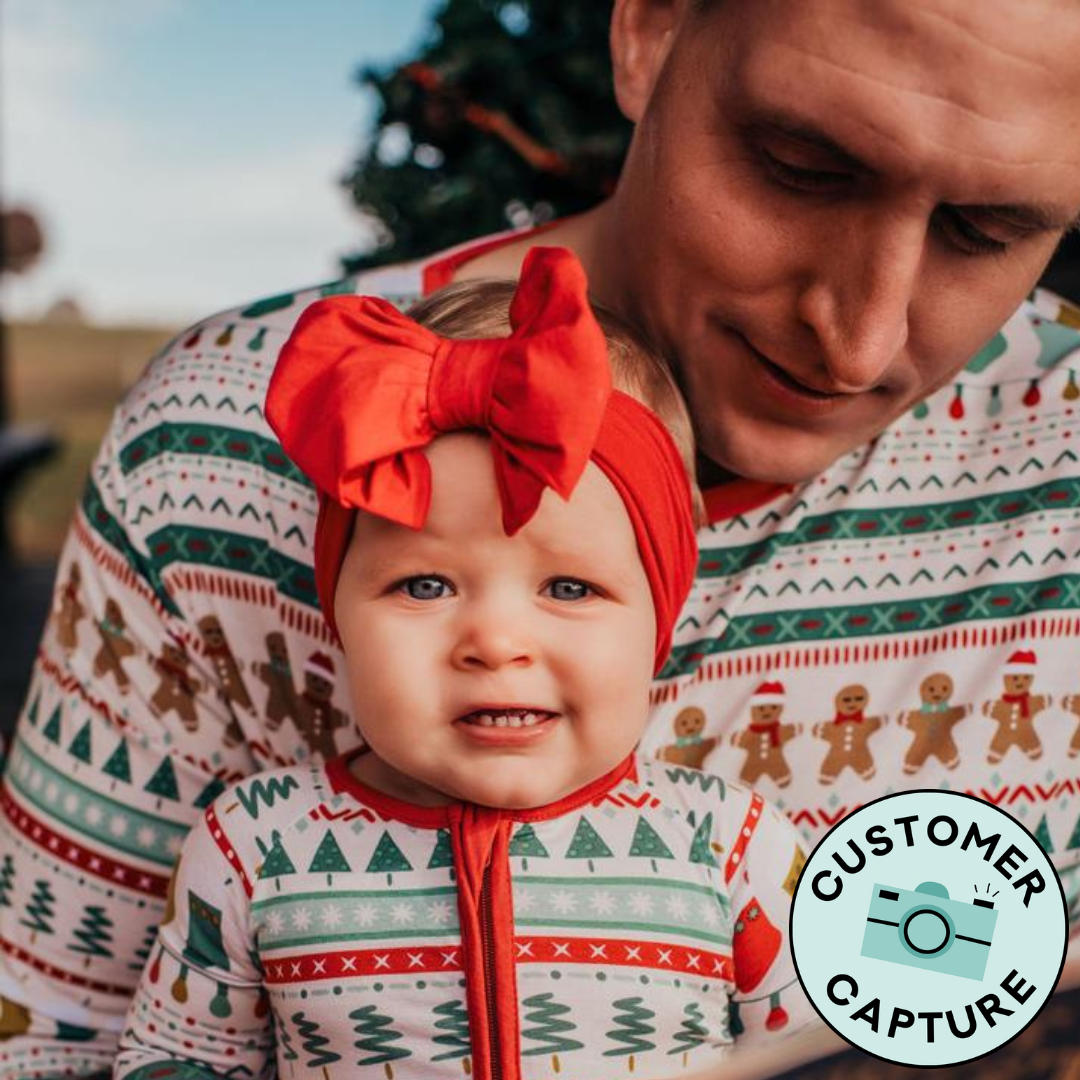 Customer capture image of a dad holding his child wearing matching Fair Isle pajamas. Dad is wearing a men's Fair Isle pajama top and child is wearing a matching zippy
