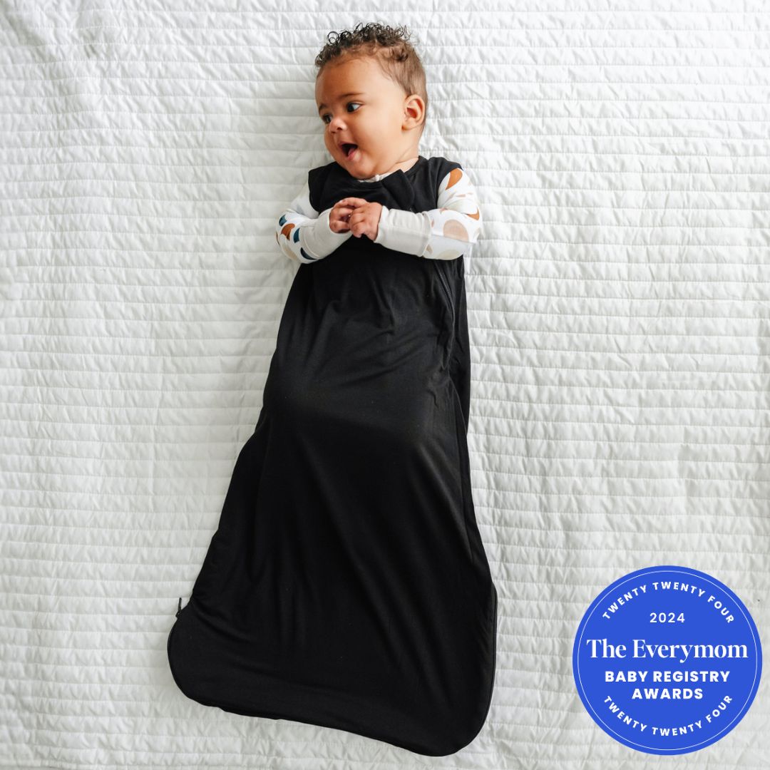 Child laying on a blanket wearing a Black sleepy bag and coordinating zippy