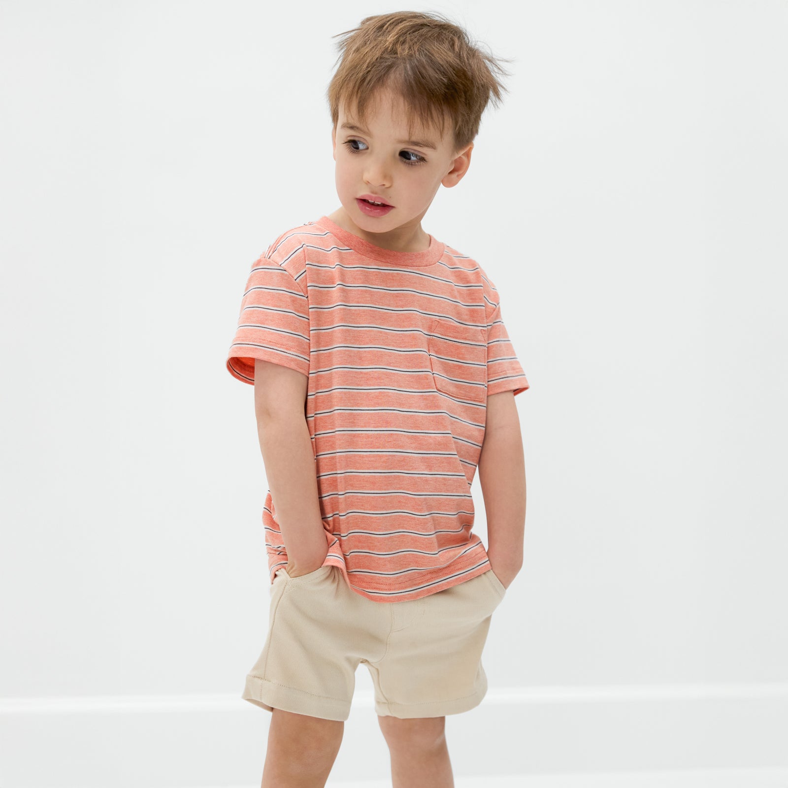 Child wearing the Coral Stripes Relaxed Pocket Tee and light khaki chino shorts