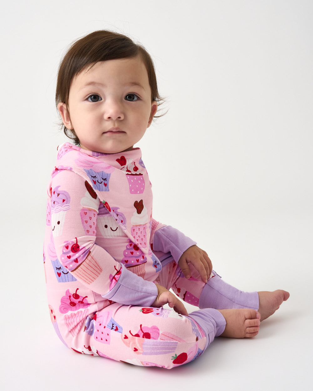 Sitting baby wearing the Cupcake Kisses Bandana Bib and matching zippy