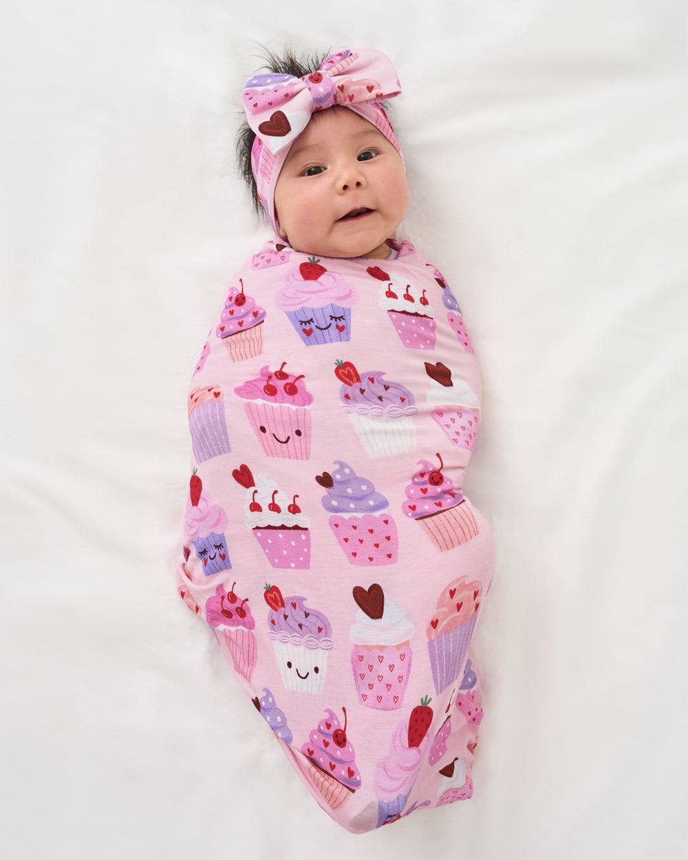 Aerial view of baby swaddled in the Cupcake Kisses Swaddle & Luxe Bow Headband Set