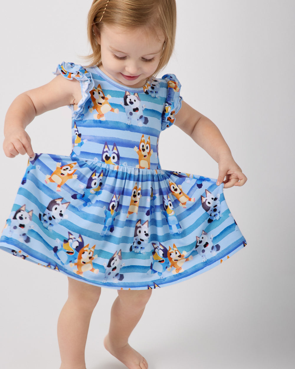 Child wearing the Bluey Dance All Day Flutter Skater Dress with Bodysuit holding out the skirt