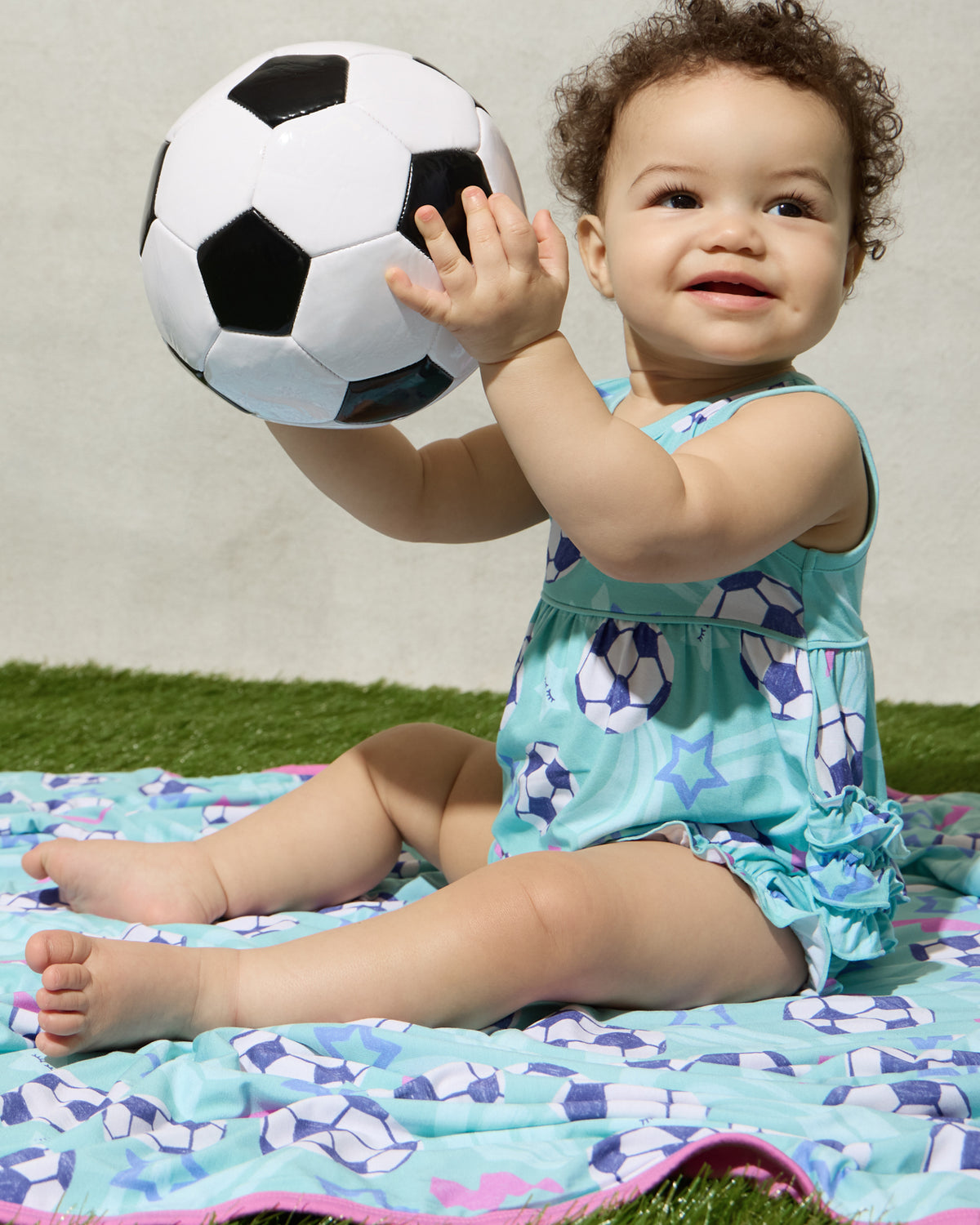 Baby wearing the Aqua Soccer Stars Bubble Romper sitting on the matching Aqua Soccer Stars blanket