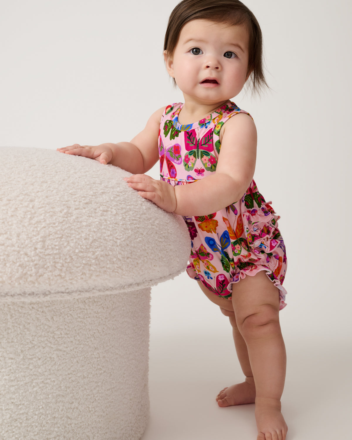 Baby leaning on a boucle ottoman wearing the Flutter Garden Bubble Romper