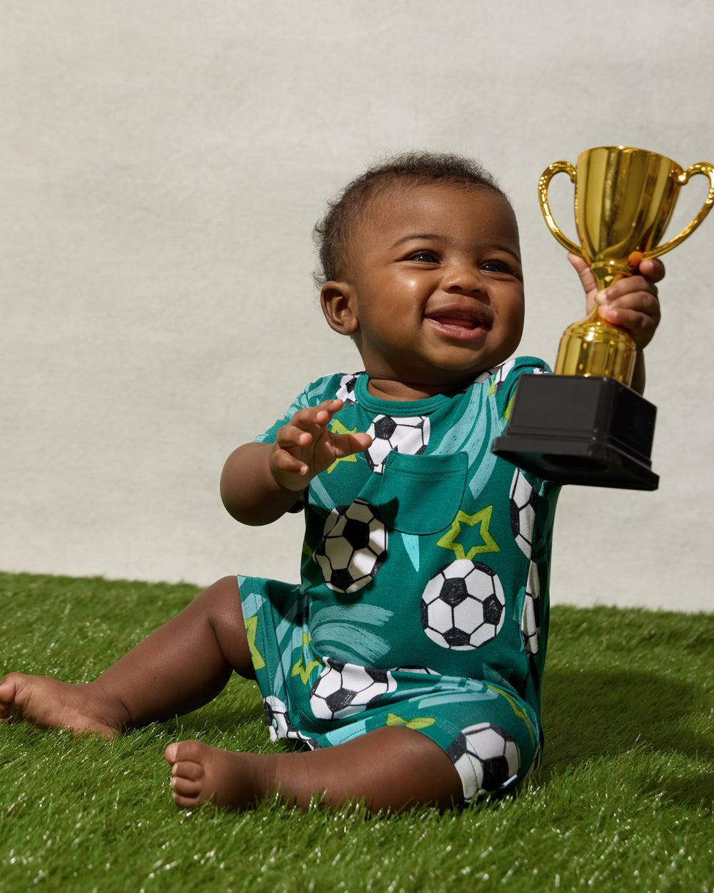 Baby holding a trophy wearing the Soccer Stars Pocket Shorty Romper